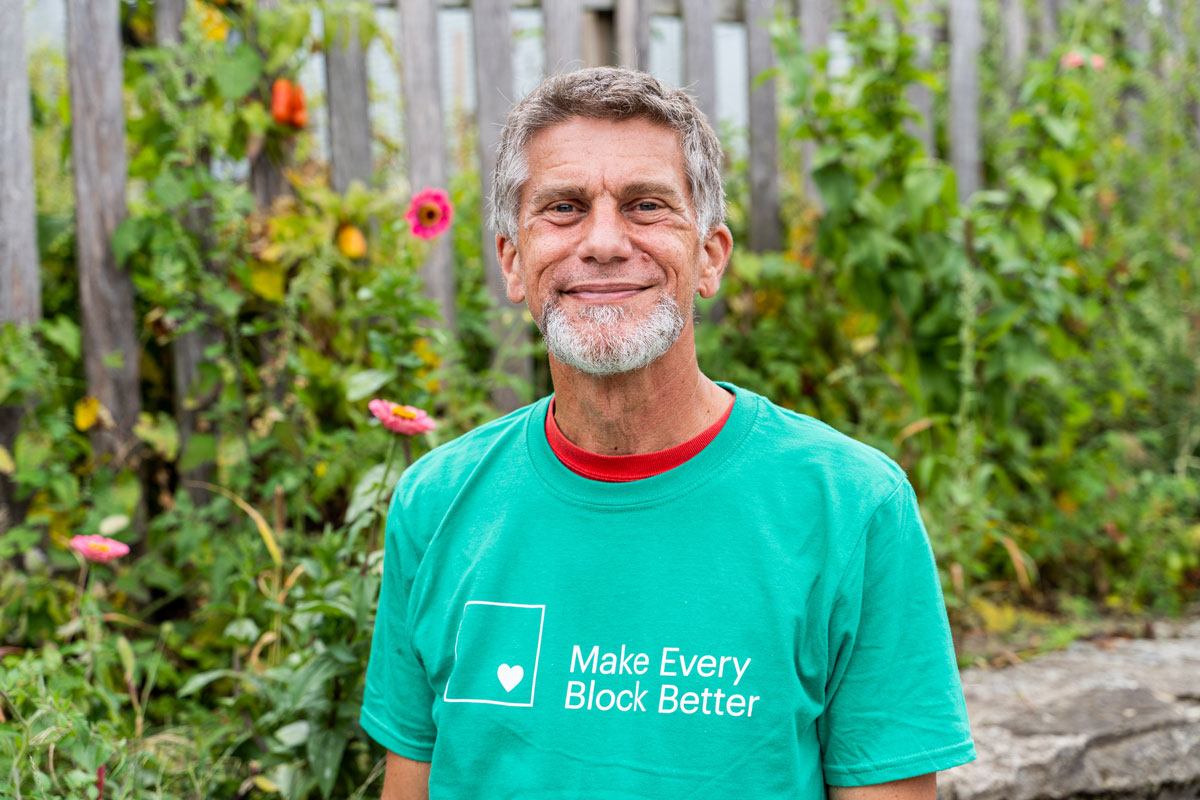 Gary Dangel wears a Make Every Block Better t-shirt while standing in front of the community garden outside Walnut Hills elementary.